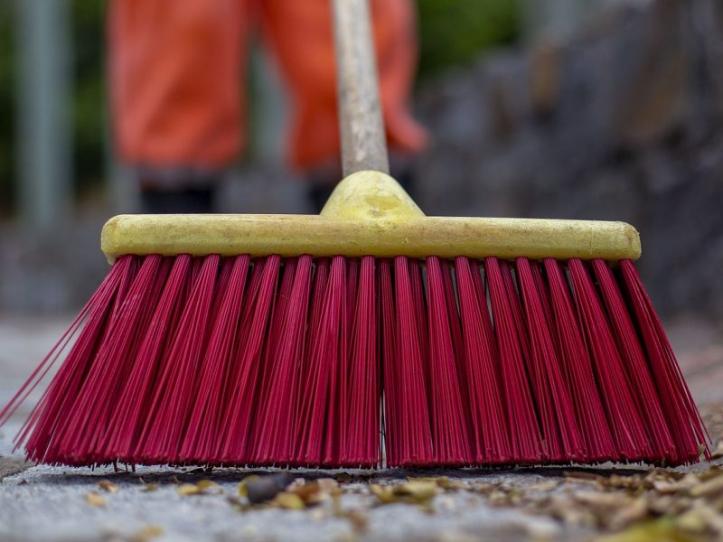 un homme avec un balai de de couleur rouge qui est entrain de nettoyer la cours